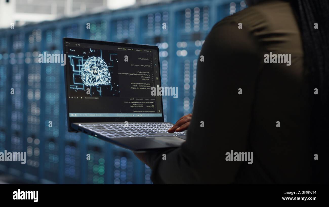 Data center engineer uses a laptop in a server room to upgrade server rigs and increase workload capacity. Stock Photo
