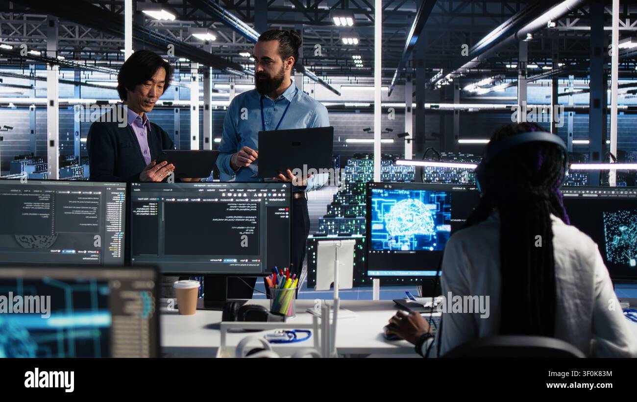 High tech server room team supervisor supervising work done by programmers working on neural network software, while supervisor overseeing IT staff members implementing deep learning tech. Stock Photo