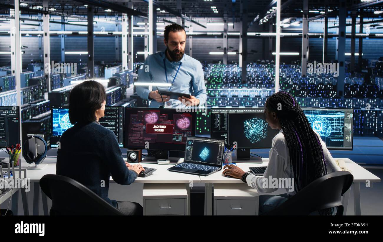 High tech server room team supervisor coordinating programmers repairing urgent system alert. Stock Photo
