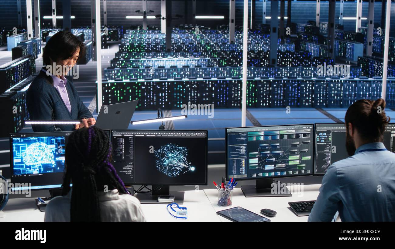 Software developers collaborating in computing facility, checking AI diagnostics on computer, while IT staff members discussing in server room, enhancing machine learning systems. Stock Photo