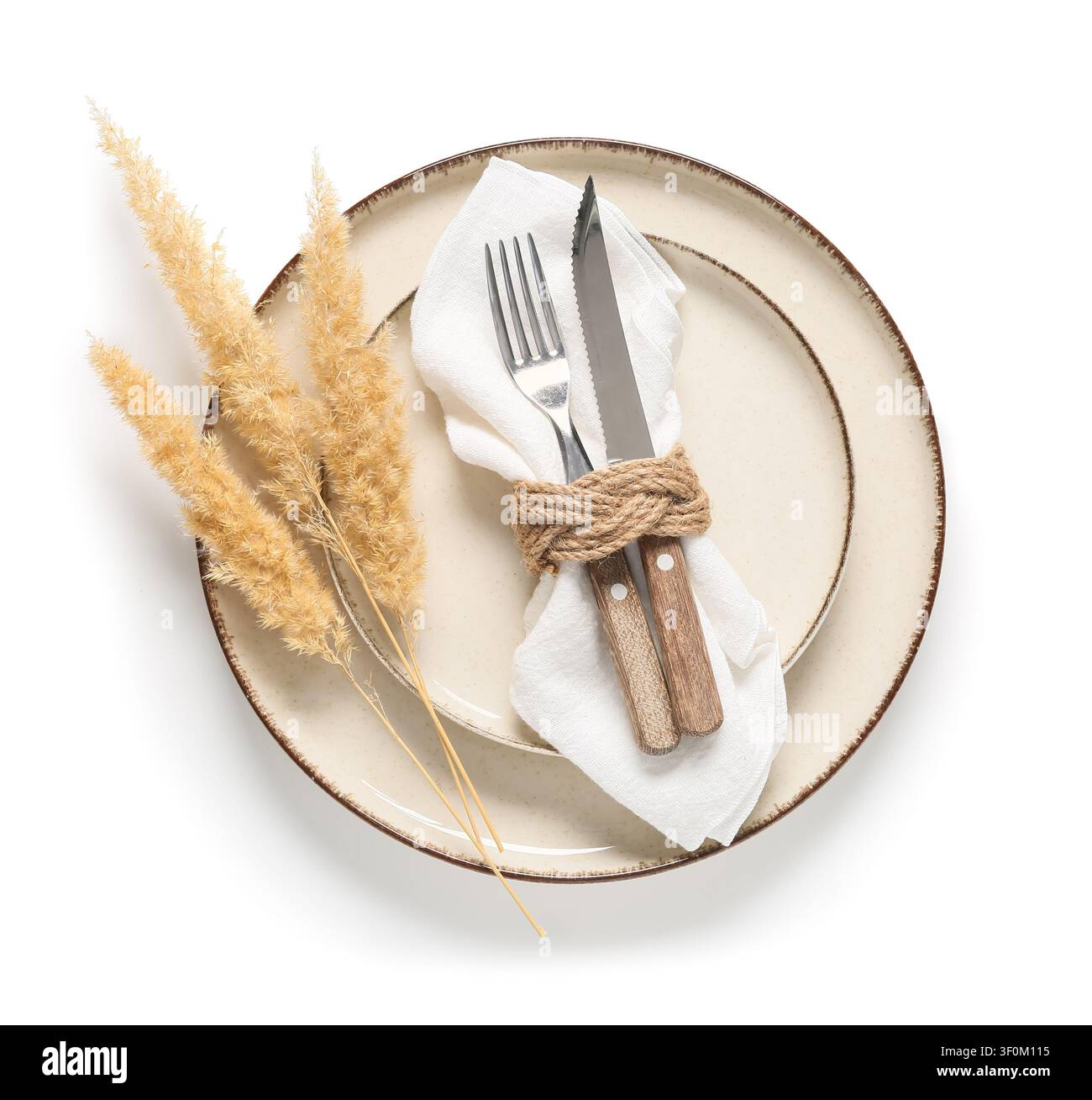 Rustic table setting with ceramic plate, white napkin, cutlery, and dried pampas grass on a white background Stock Photo