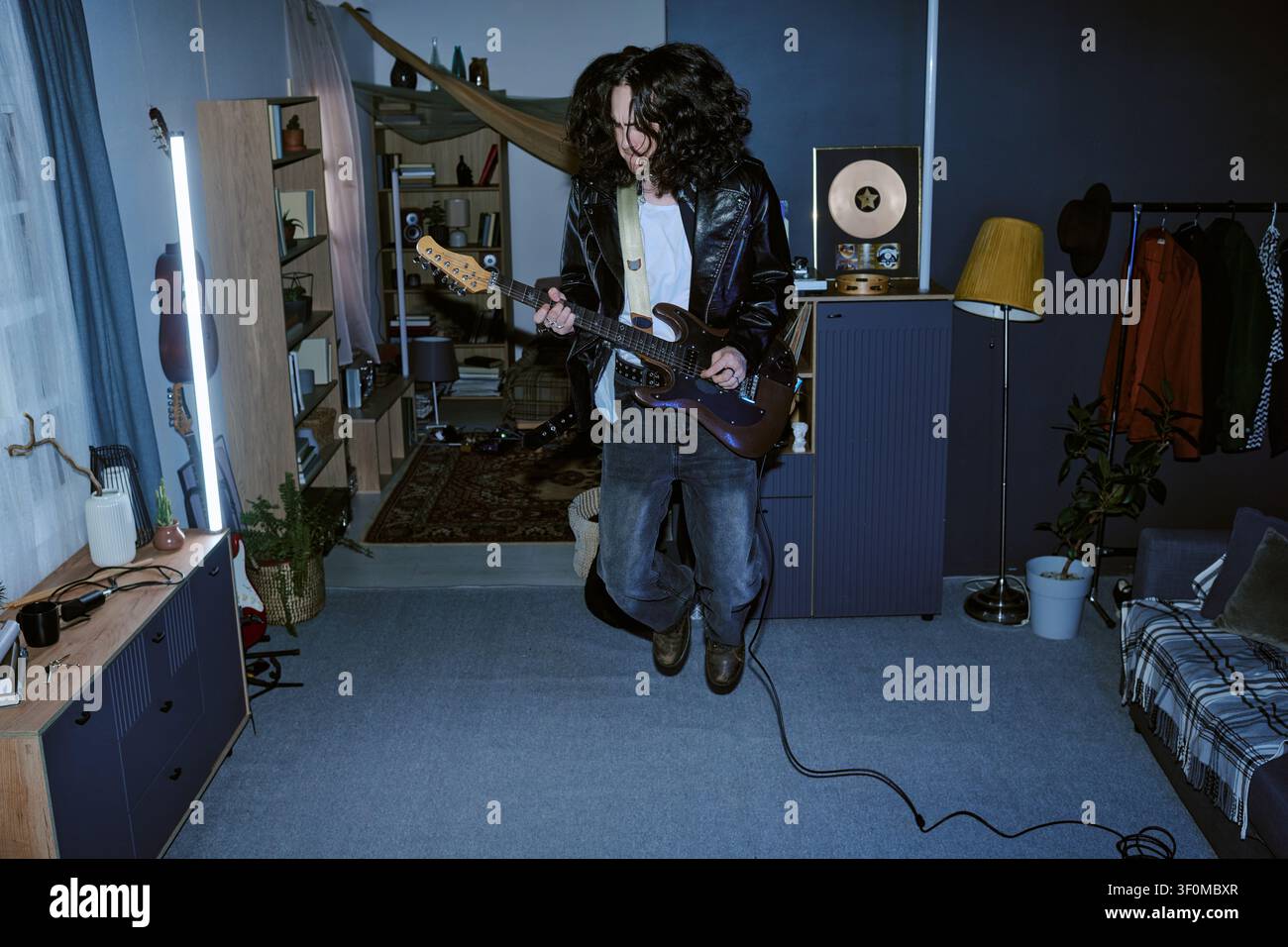 Man Jumping While Playing Electric Guitar at Home for Promotion Stock Photo