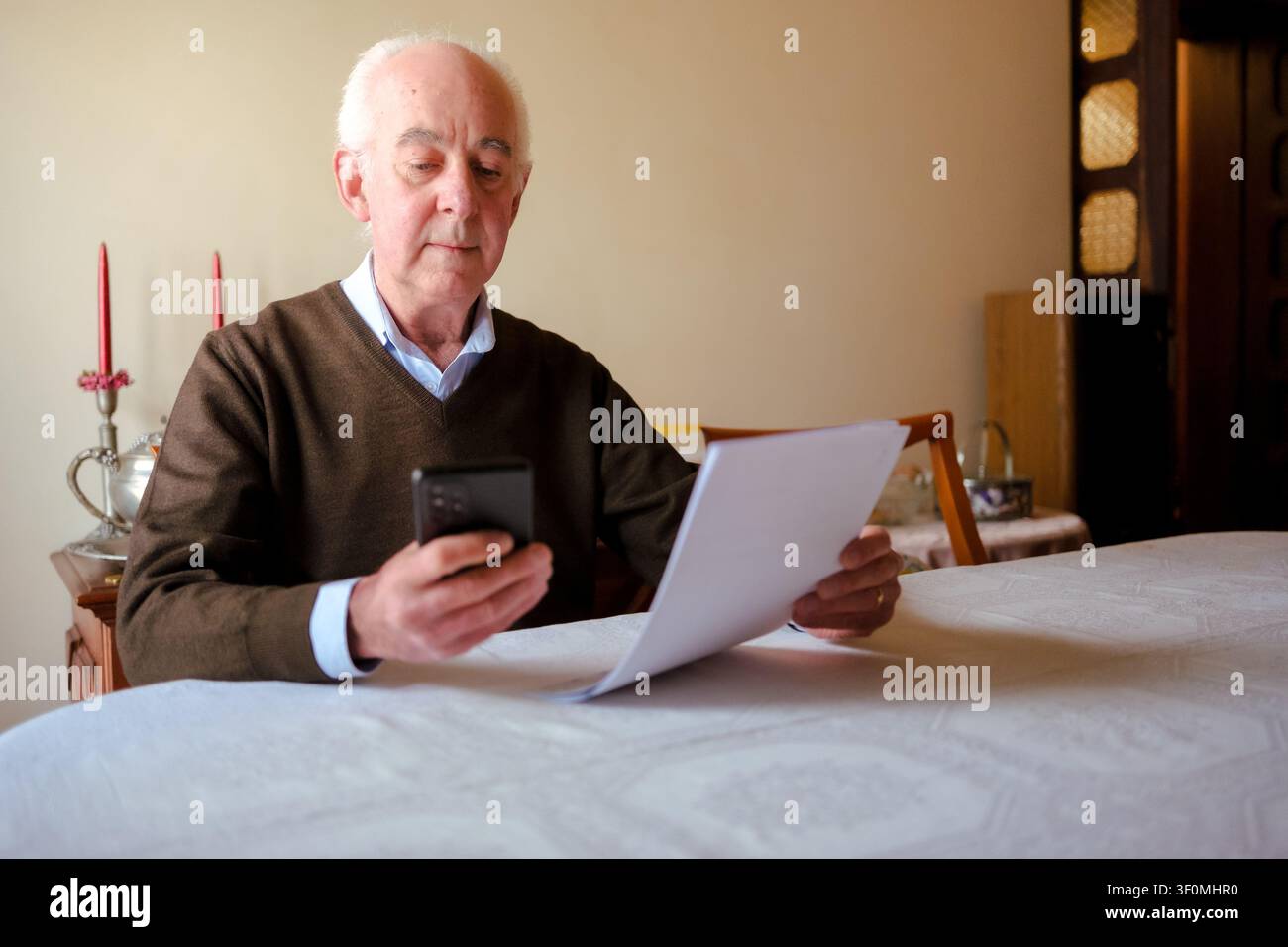 Senior man checking financial documents while using a mobile phone at home Stock Photo