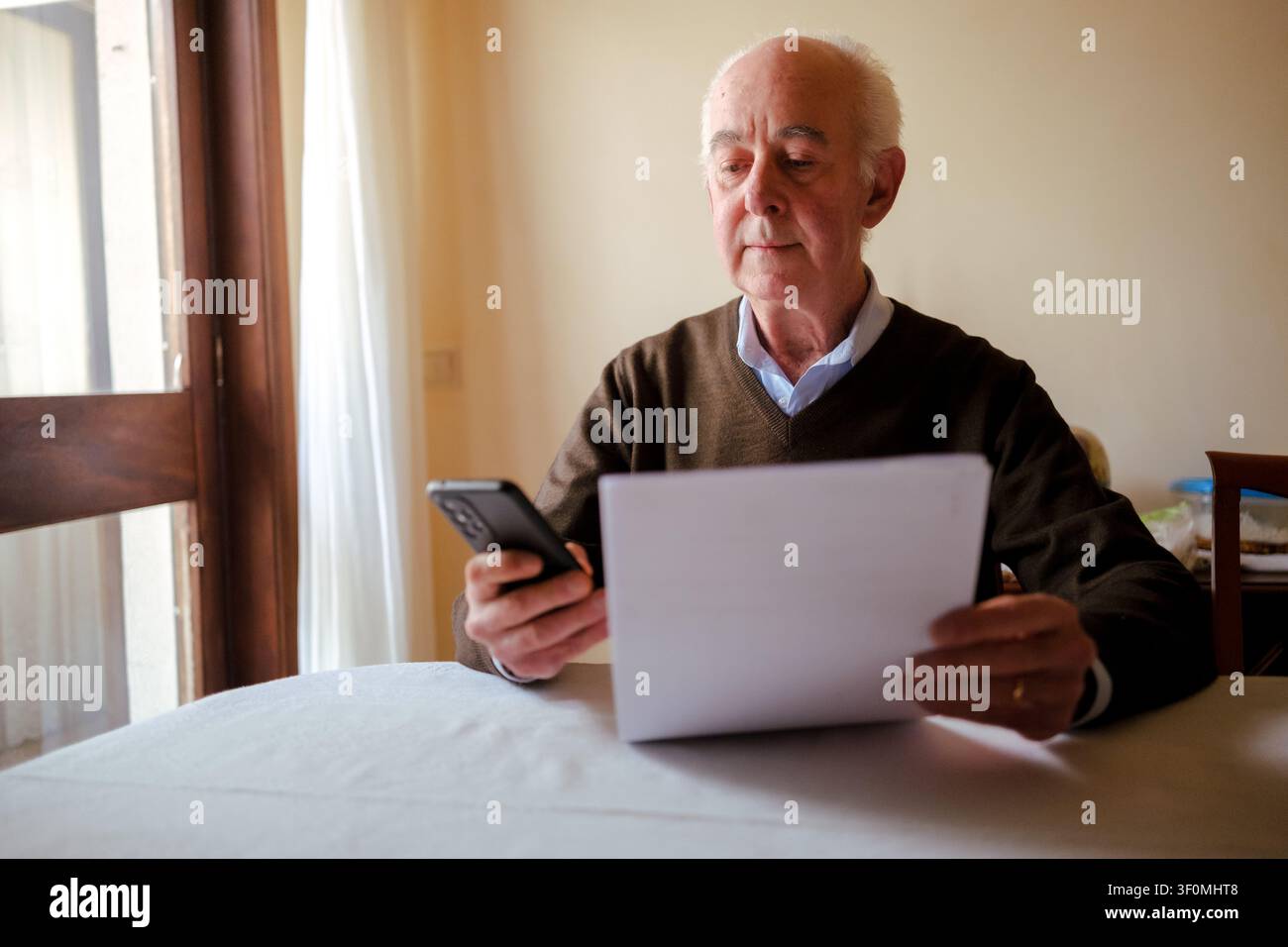 Senior man using smartphone while working with documents at a table Stock Photo