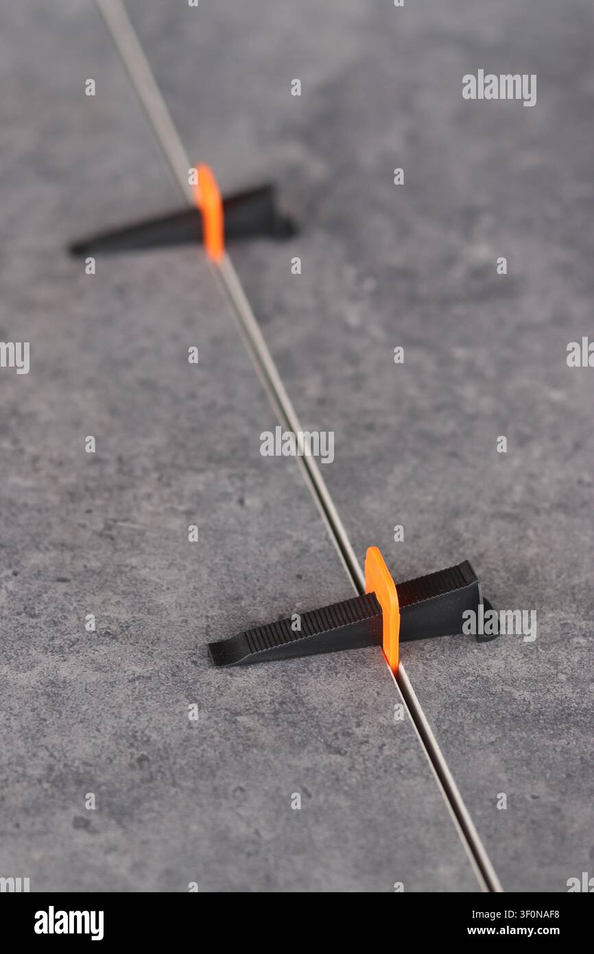 Professional tile leveling system. The process of laying porcelain tiles using a plastic orange clamp and a black wedge to create a perfectly even sea Stock Photo