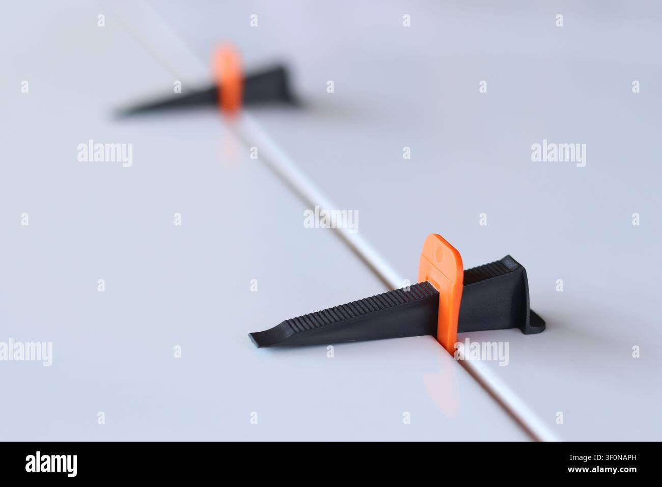 Using a plastic wedge and a clamp of a tile leveling system during repair. Professional laying of ceramic tiles on the floor. The process of leveling Stock Photo