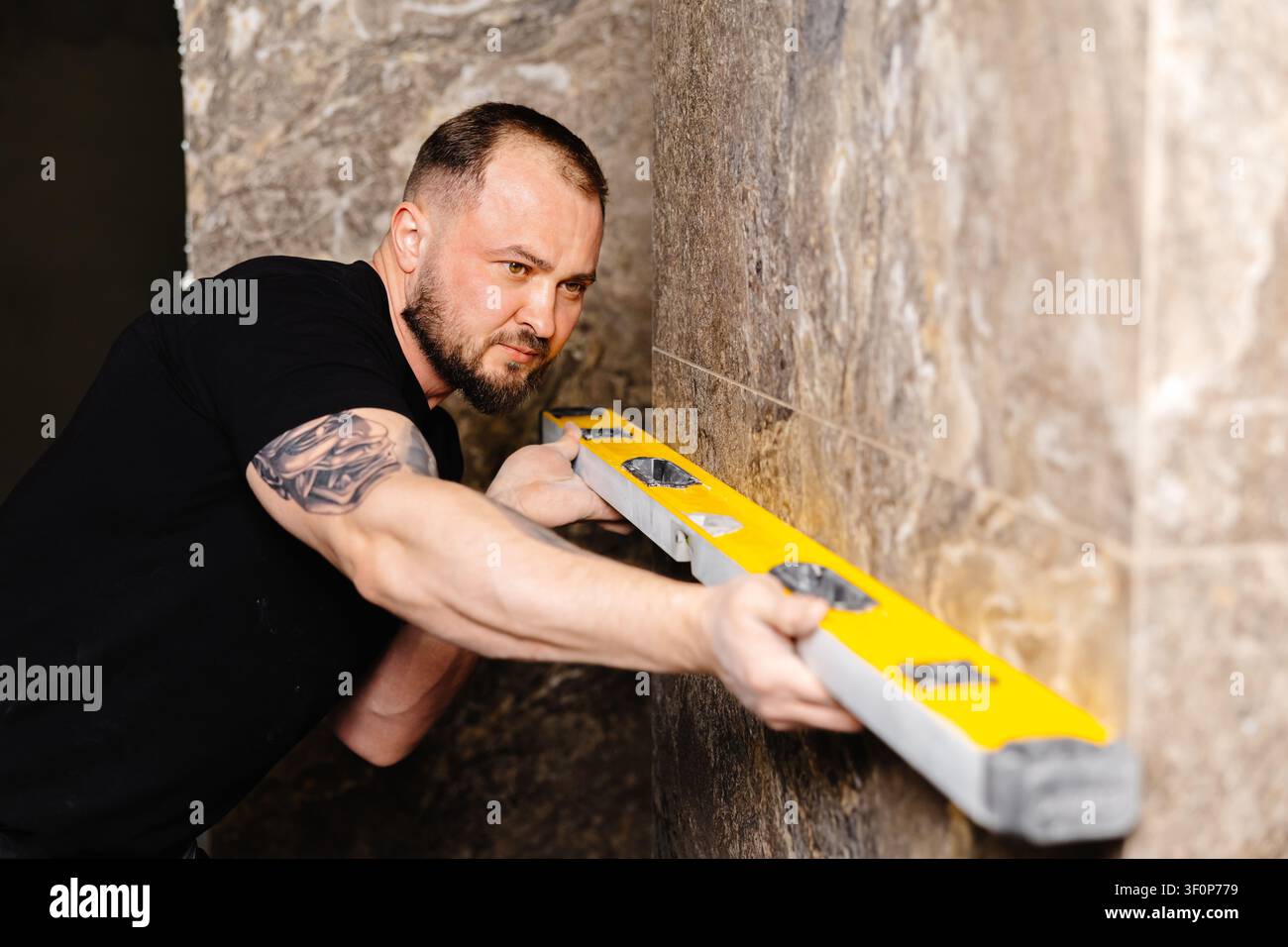 Builder checking the evenness of marble tiles with a level tool, ensuring precision and accuracy during renovation work on a wall Stock Photo