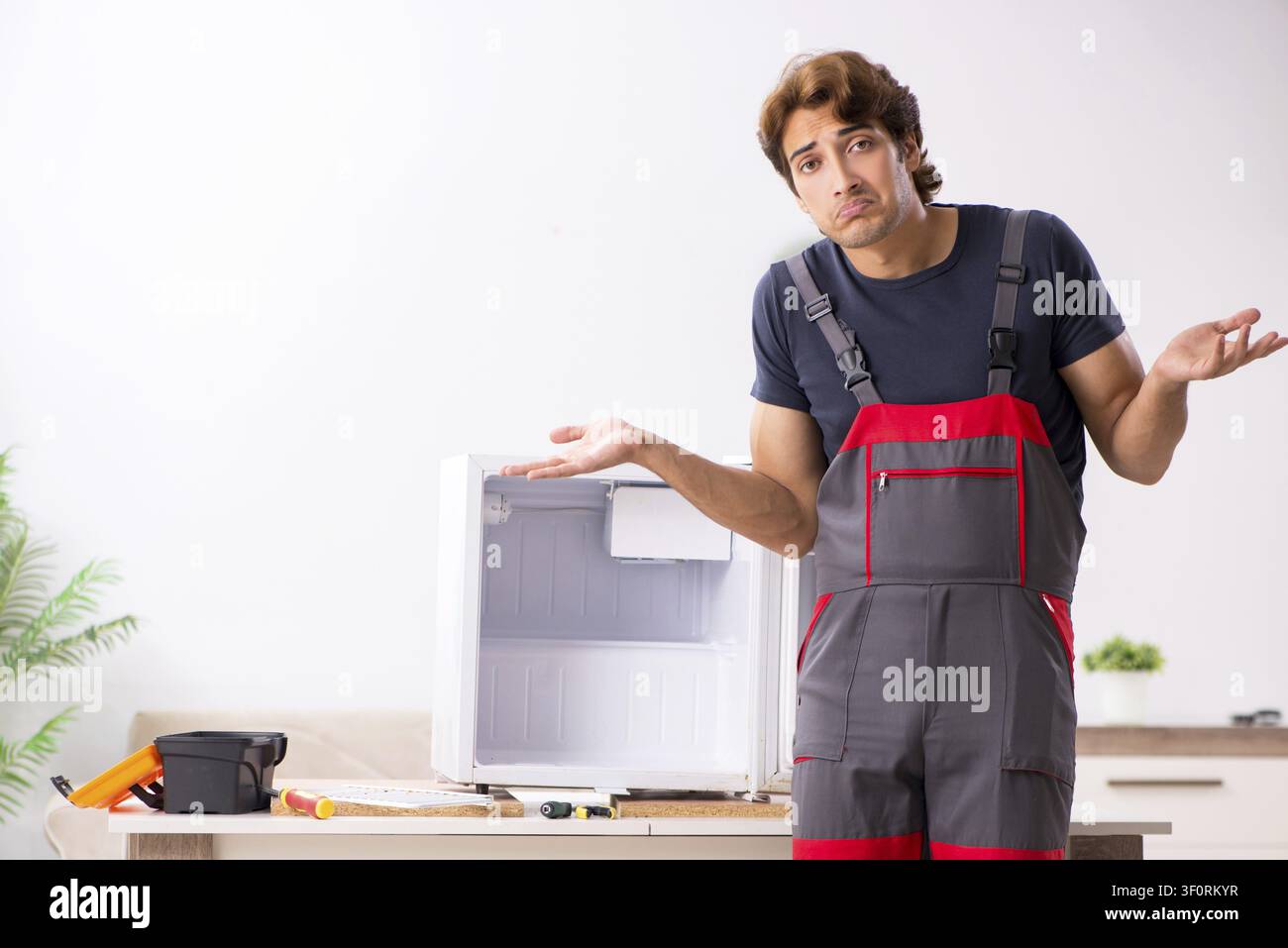 Young handsome contractor repairing fridge Stock Photo