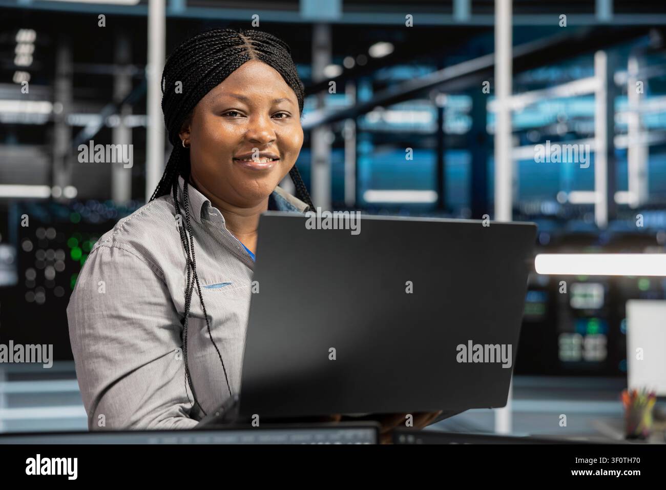 Cheerful server facility software engineer applying AI neural network models. Cheerful server environment staff member works with AI programming tools on workstation, setting up specialized hardware. Stock Photo