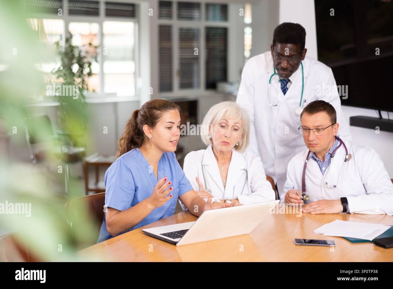 Doctors sitting around the table looking at the notebook Stock Photo