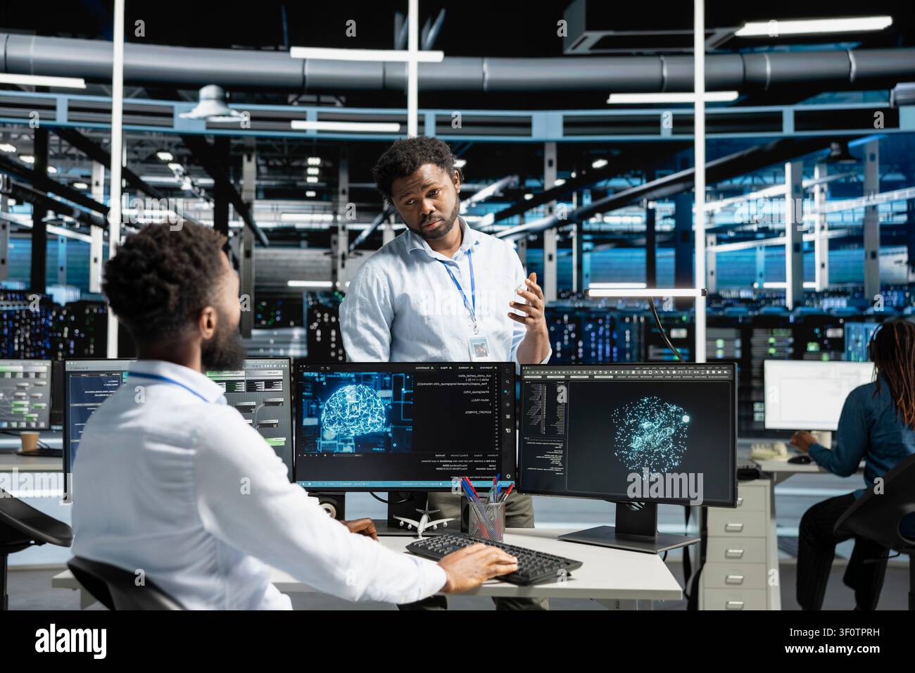 Server room manager supervising work done by engineer working with deep learning models to review data sets. Stock Photo