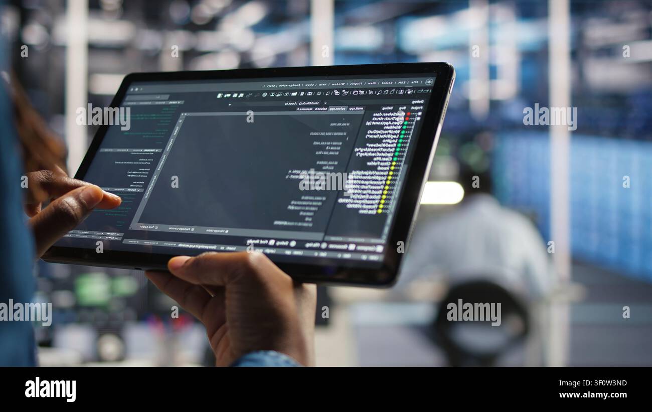 Data center programmer uses a tablet to update server software, supporting reliable infrastructure operations. Stock Photo