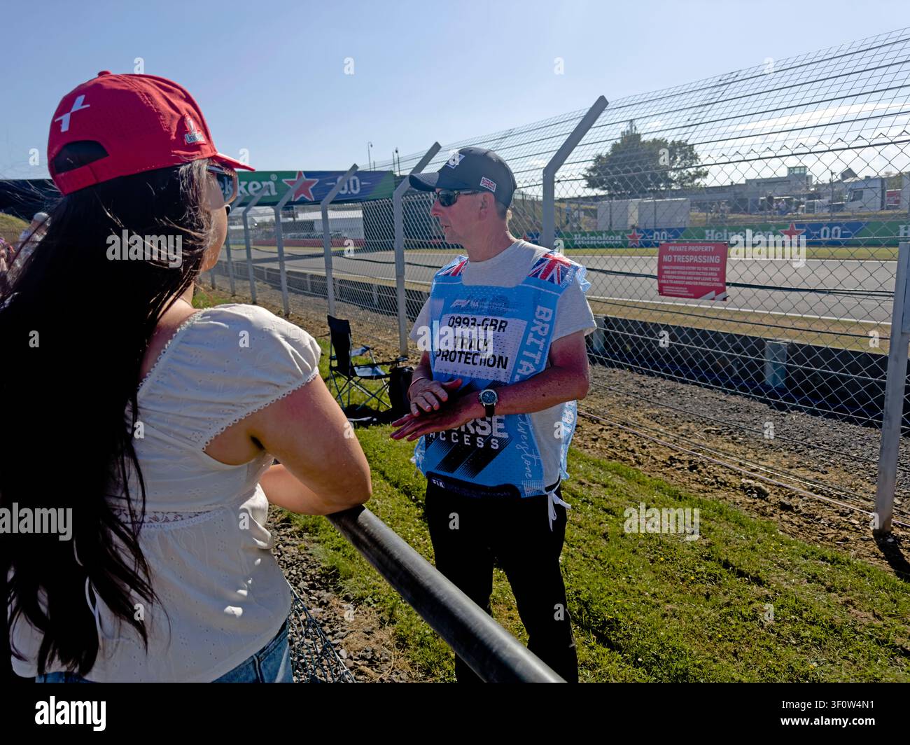 Track-access steward discusses safety with a spectator behind protective fencing at the 2026 British Grand Prix, F1 GP Silverstone circuit Stock Photo