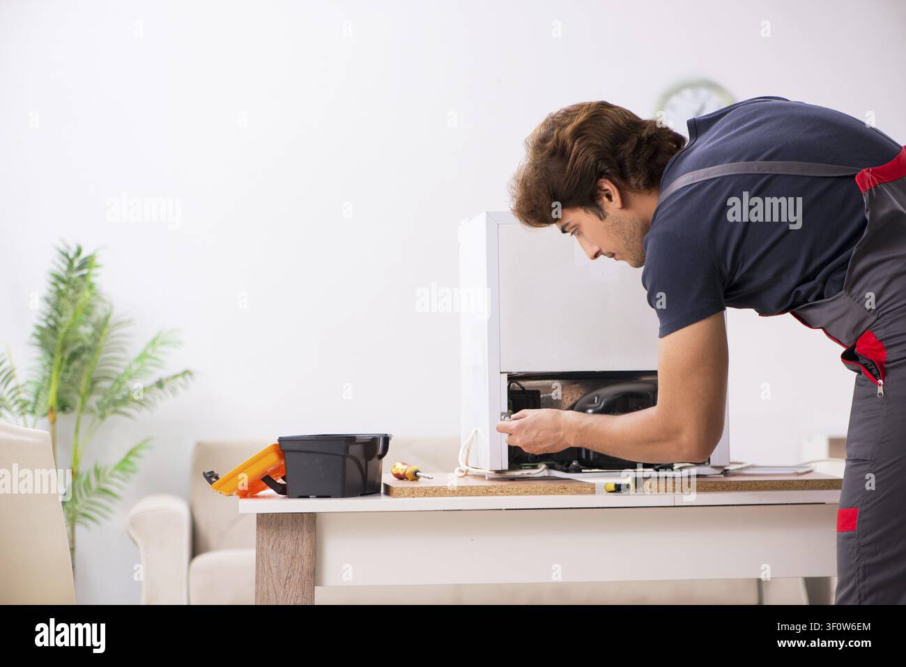Young handsome contractor repairing fridge Stock Photo