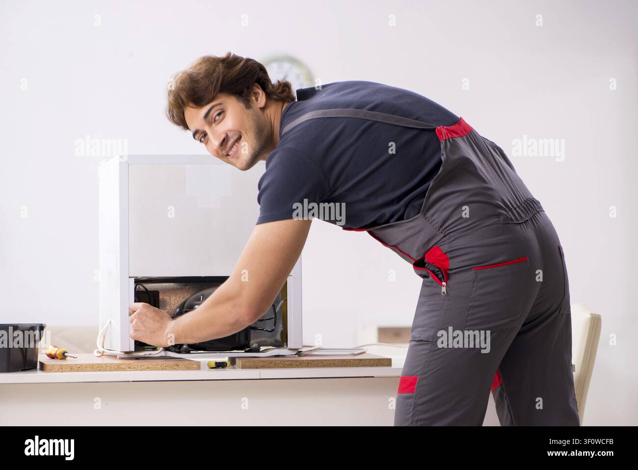 Young handsome contractor repairing fridge Stock Photo