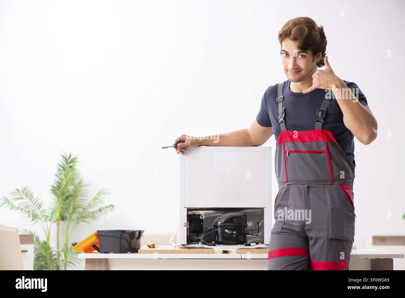 Young handsome contractor repairing fridge Stock Photo