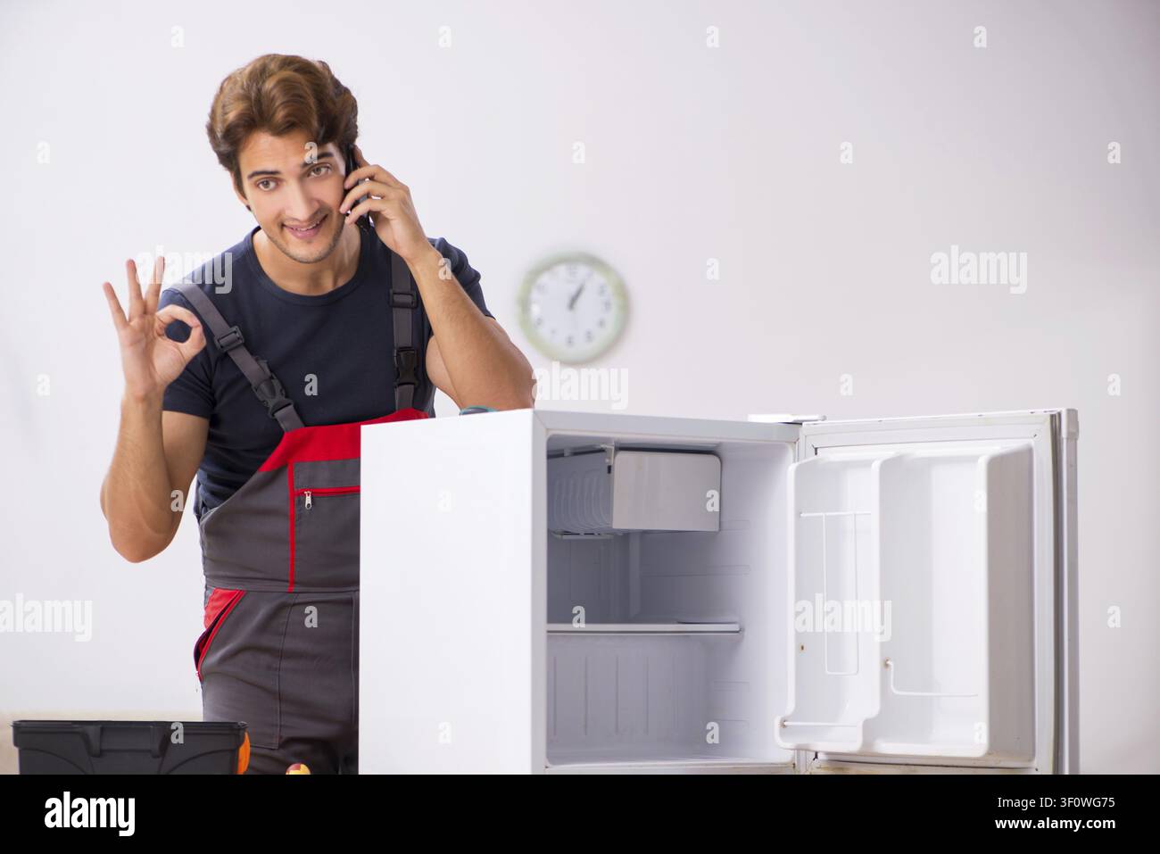 Young handsome contractor repairing fridge Stock Photo