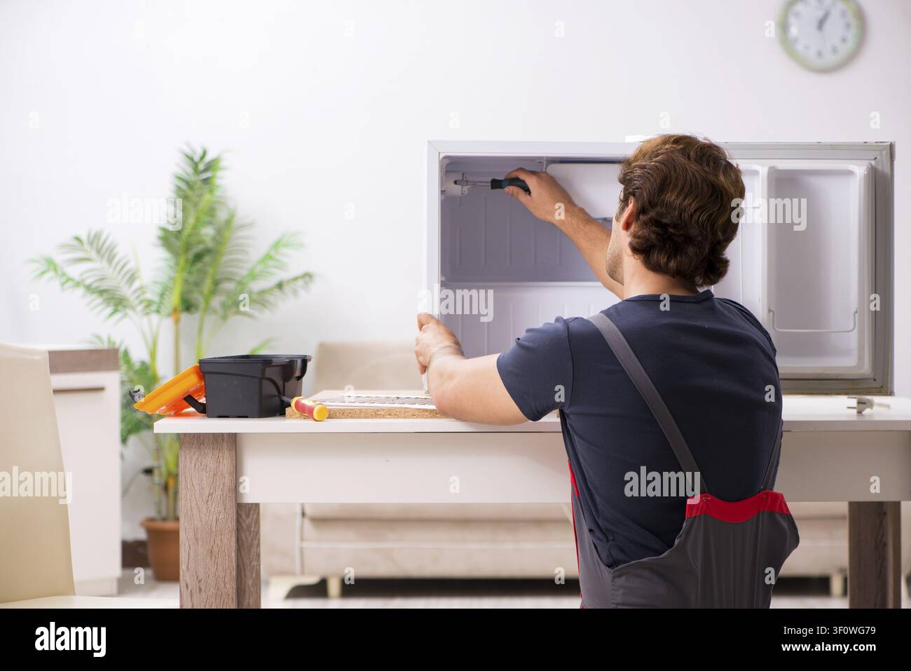 Young handsome contractor repairing fridge Stock Photo
