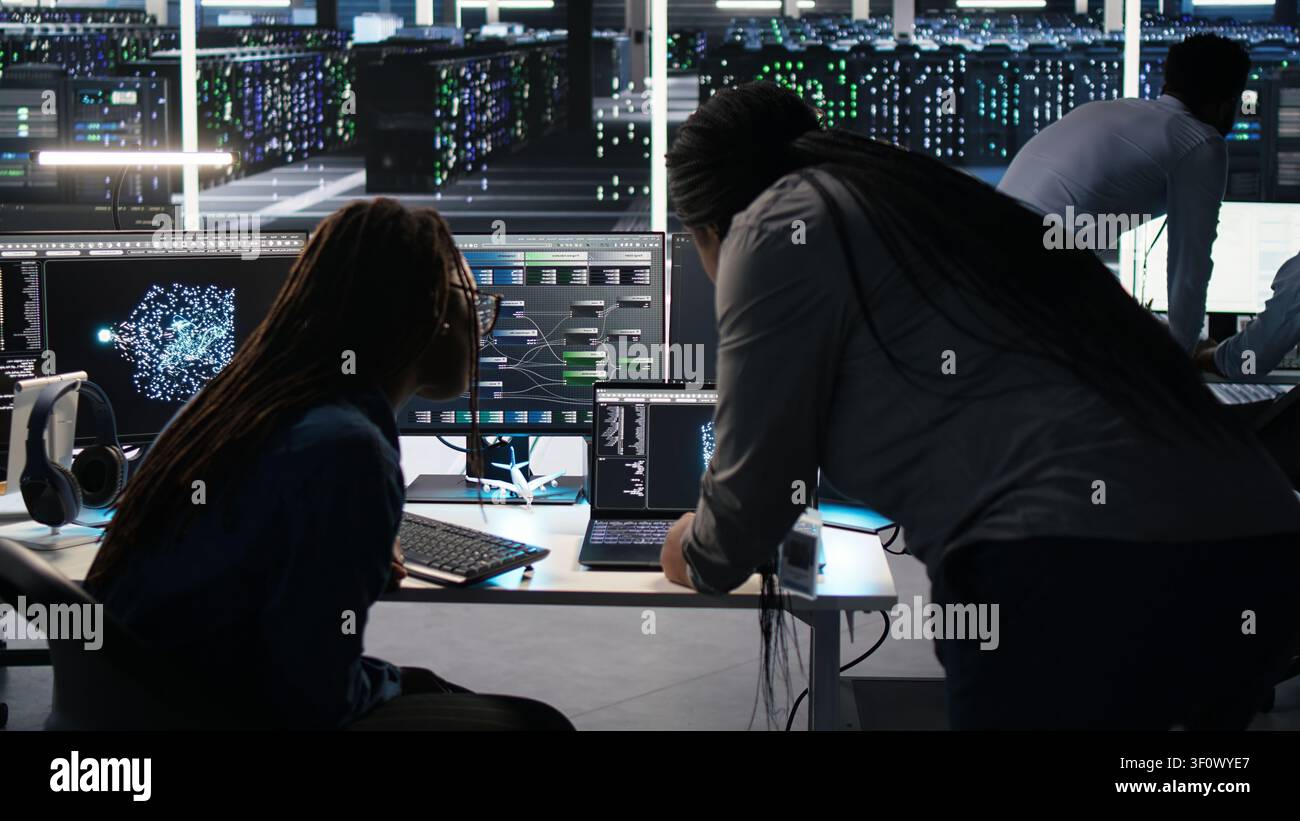High tech server room collaborative team members work with visual programming workflow to detect equipment operational performance issues with engineering team team members check data analysis graph. Stock Photo