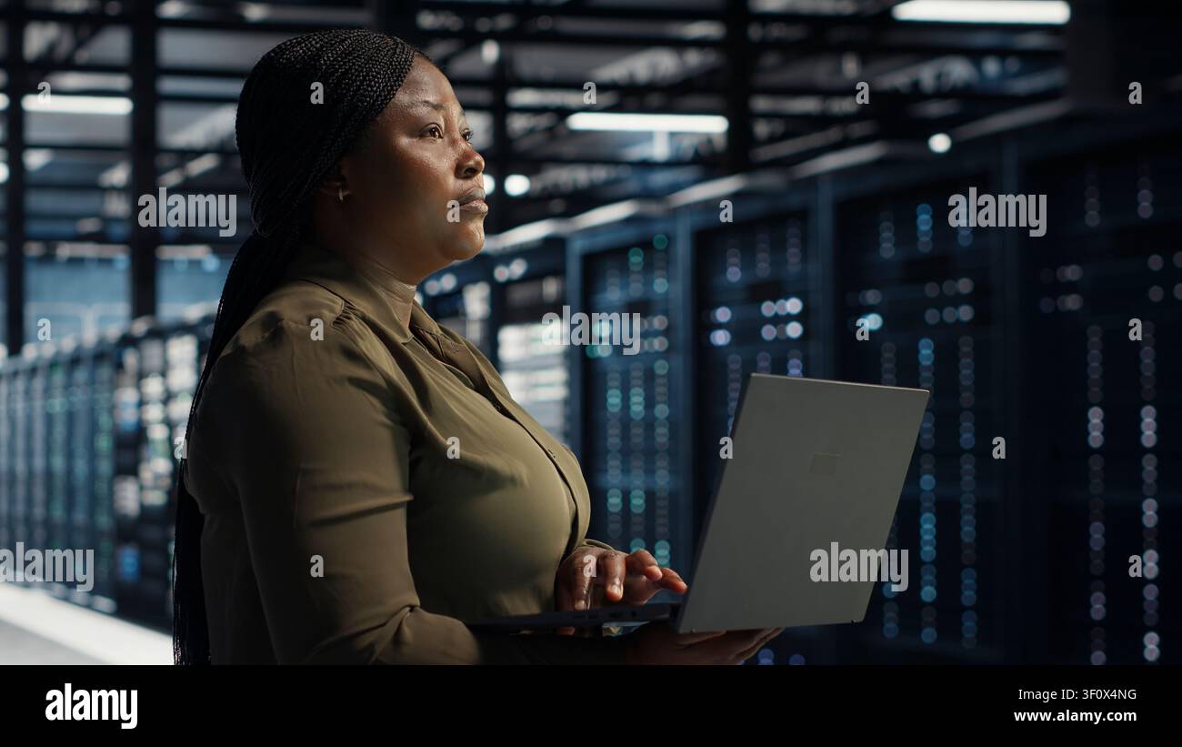 Software engineer in server facility working with notebook computer to update systems for increased stability. Stock Photo