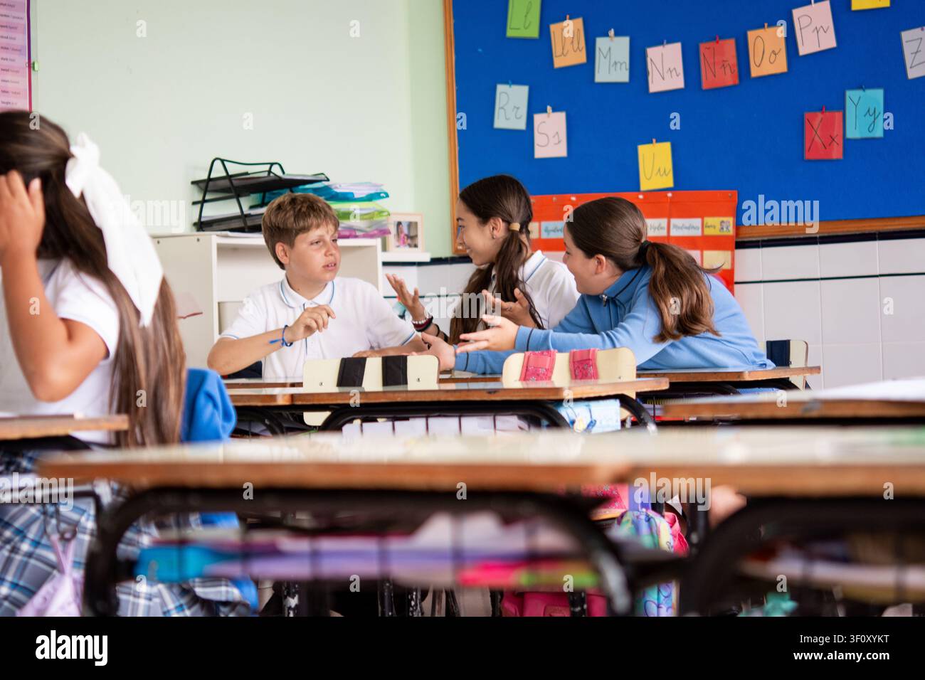 Elementary school classmates talking and collaborating during a lesson in a bright classroom. Stock Photo