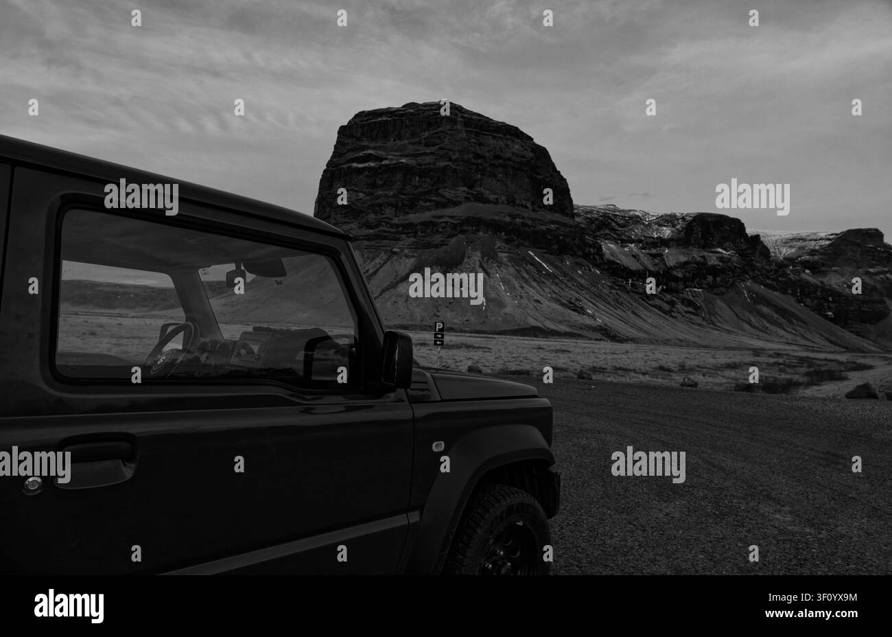 4x4 stands on Iceland's winter moorland, dwarfed by the dramatic volcanic dome of Lómagnúpur in b&w Stock Photo
