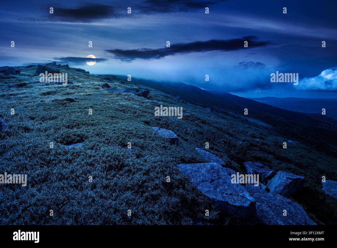 nature scenery with mountain under summer sky at night. full moon over alpine landscape of carpathian mountain with grassy slopes. low fluffy clouds o Stock Photo