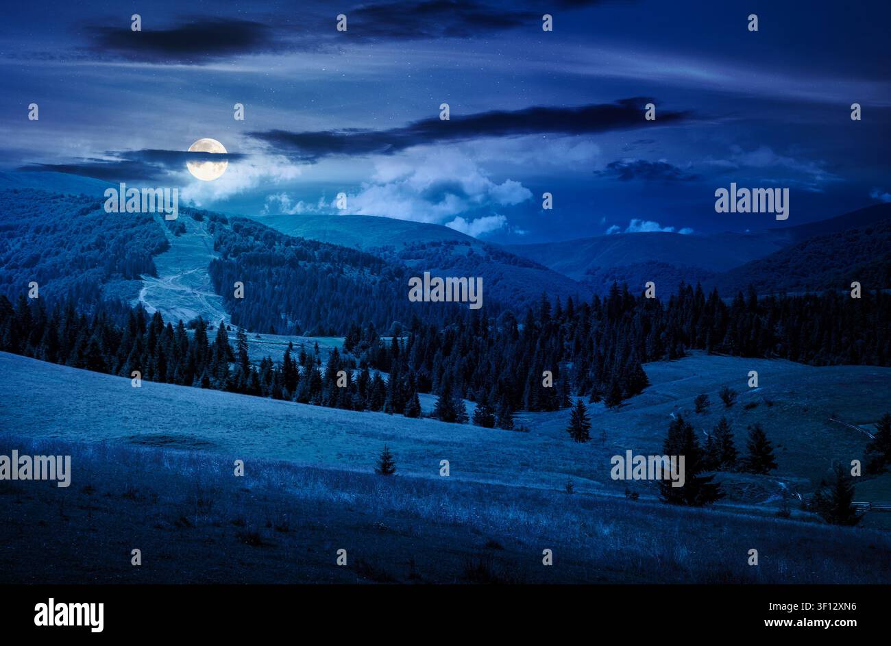 mountainous countryside landscape on summer night. full moon over view of green rural scenery with grassy pastures and rolling forested hills. mysteri Stock Photo