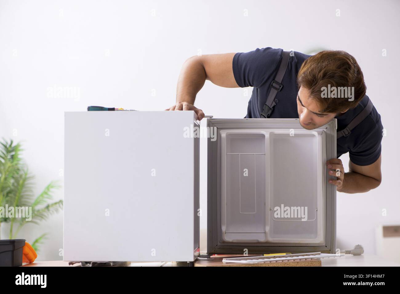 Young handsome contractor repairing fridge Stock Photo