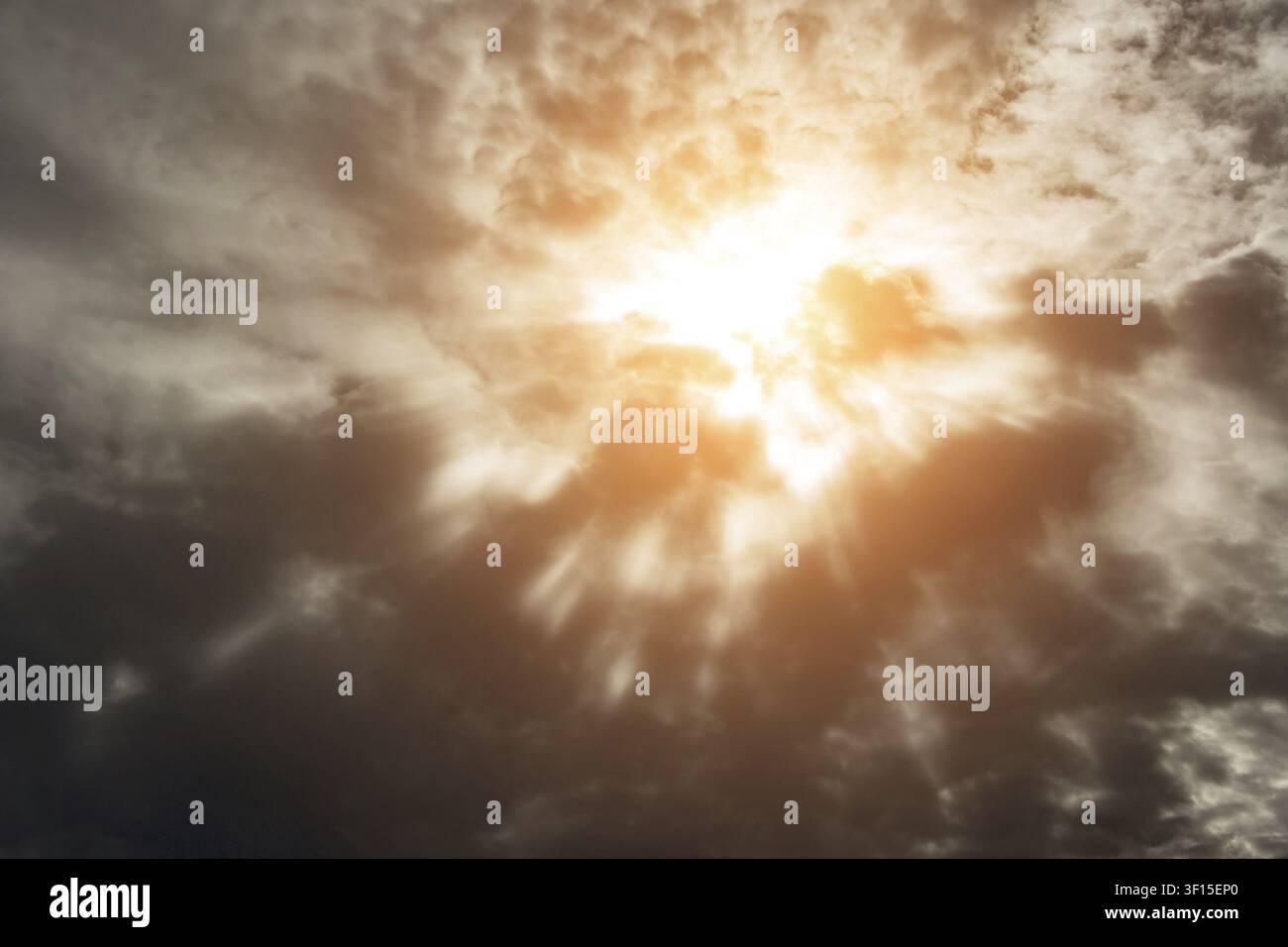 Dramatic background with warm sun rays penetrating dark clouds Stock Photo