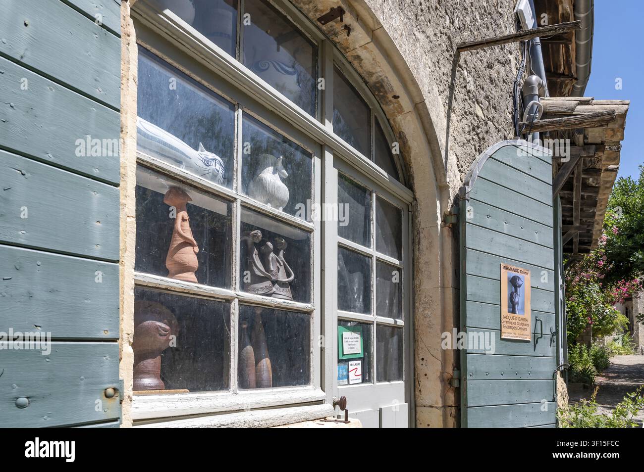 View of the shop window of an art studio and pottery studio with ceramic sculptures and clay figures on display behind lattice windows next to open, p Stock Photo