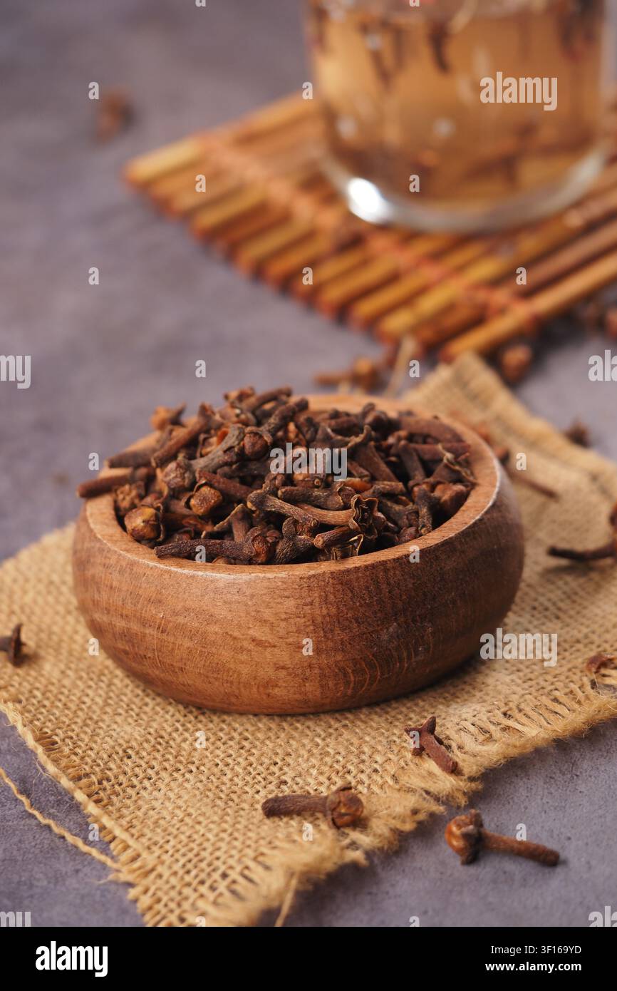 Rich cloves resting in a wooden bowl on a textured surface Stock Photo