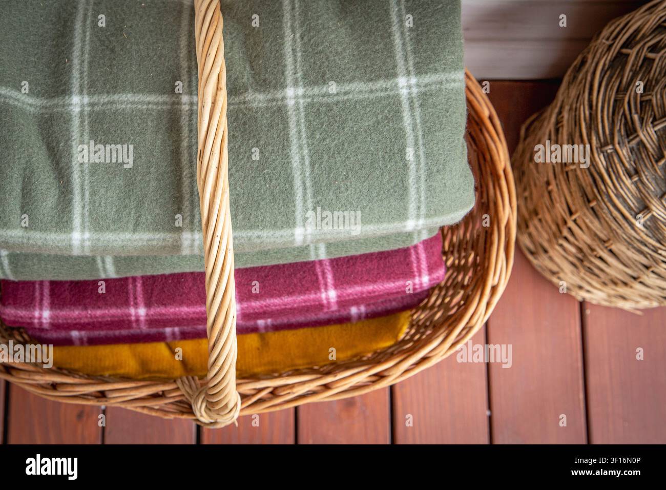 Folded wool blankets in wicker basket creating cozy rustic home interior storage Stock Photo