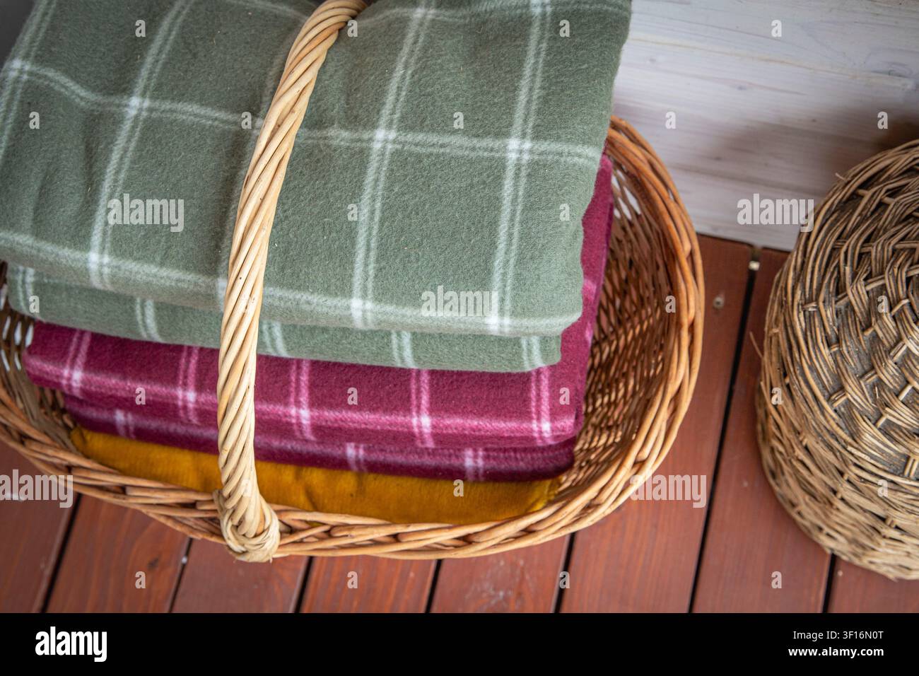 Folded wool blankets in wicker basket creating cozy rustic home interior storage Stock Photo