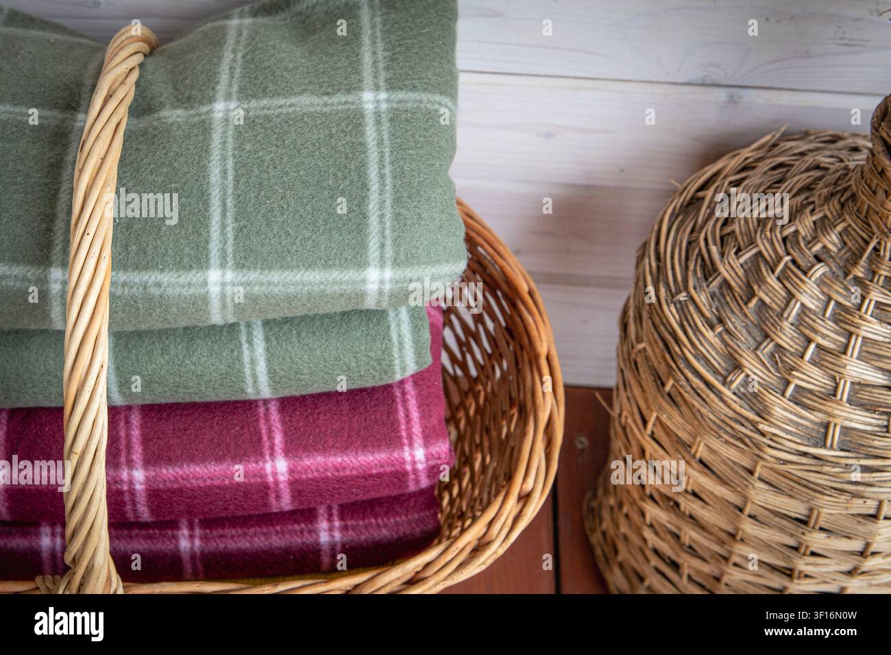 Folded wool blankets in wicker basket creating cozy rustic home interior storage Stock Photo