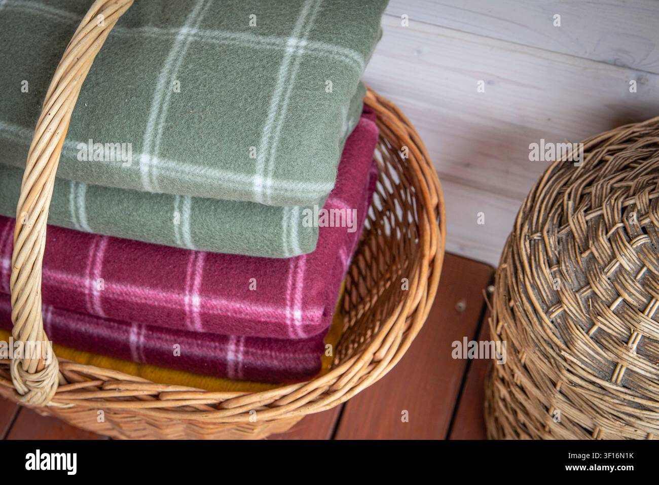 Folded wool blankets in wicker basket creating cozy rustic home interior storage Stock Photo