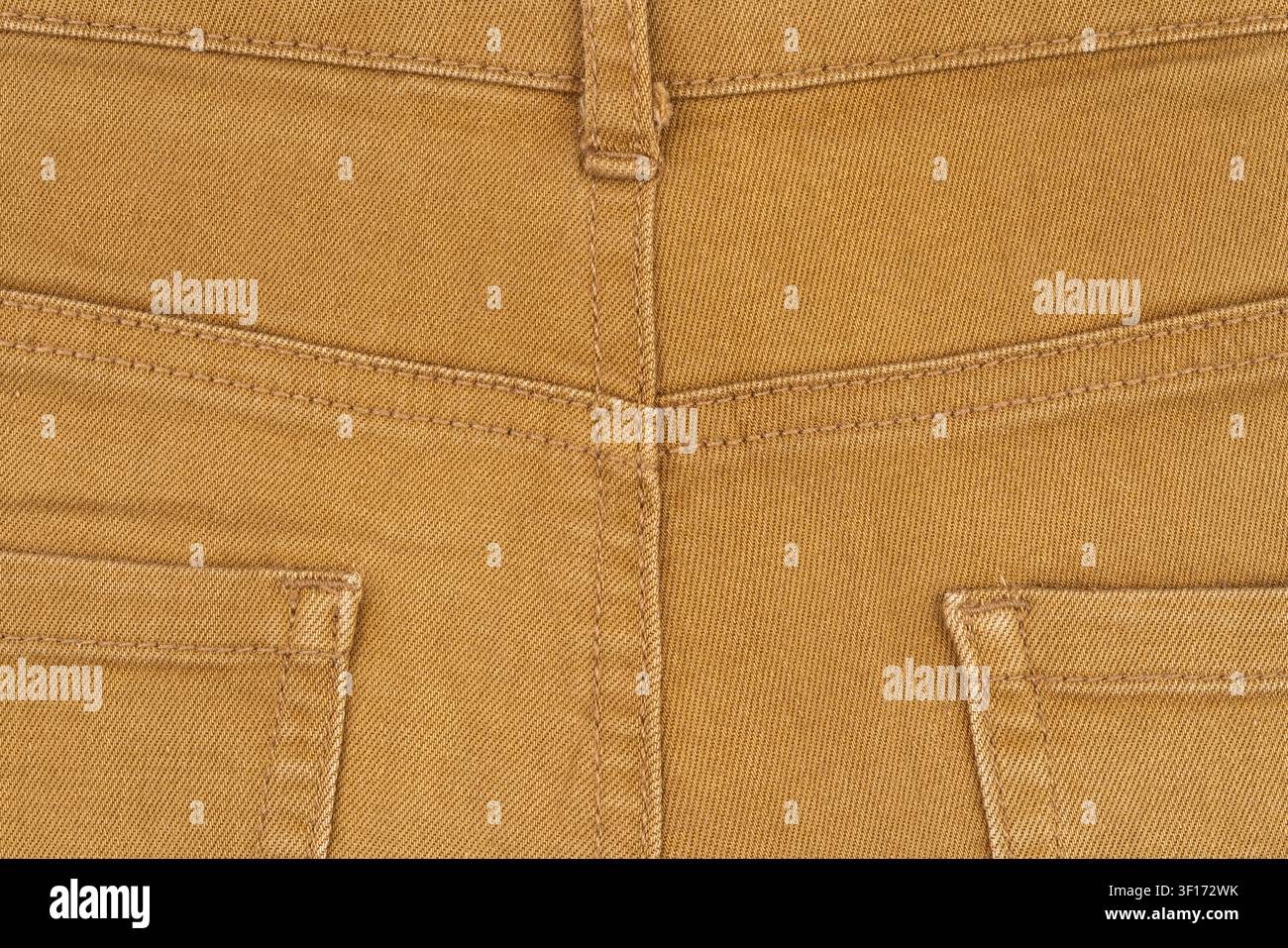 Close up detail of brown mustard color denim pants. Back view showing pockets, yoke, belt loop and stitching. Flat lay composition highlights fabric t Stock Photo
