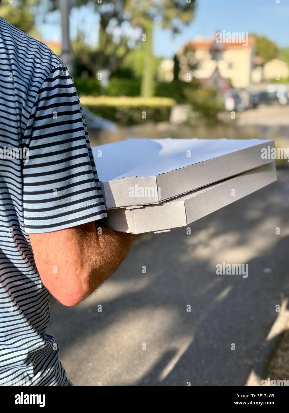 Rear view of a man walking along a street carrying two pizza boxes Stock Photo