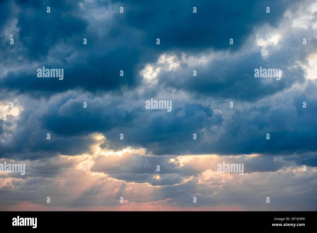 Dramatic sky with clouds and sunlight breaking through at sunset. Stock Photo