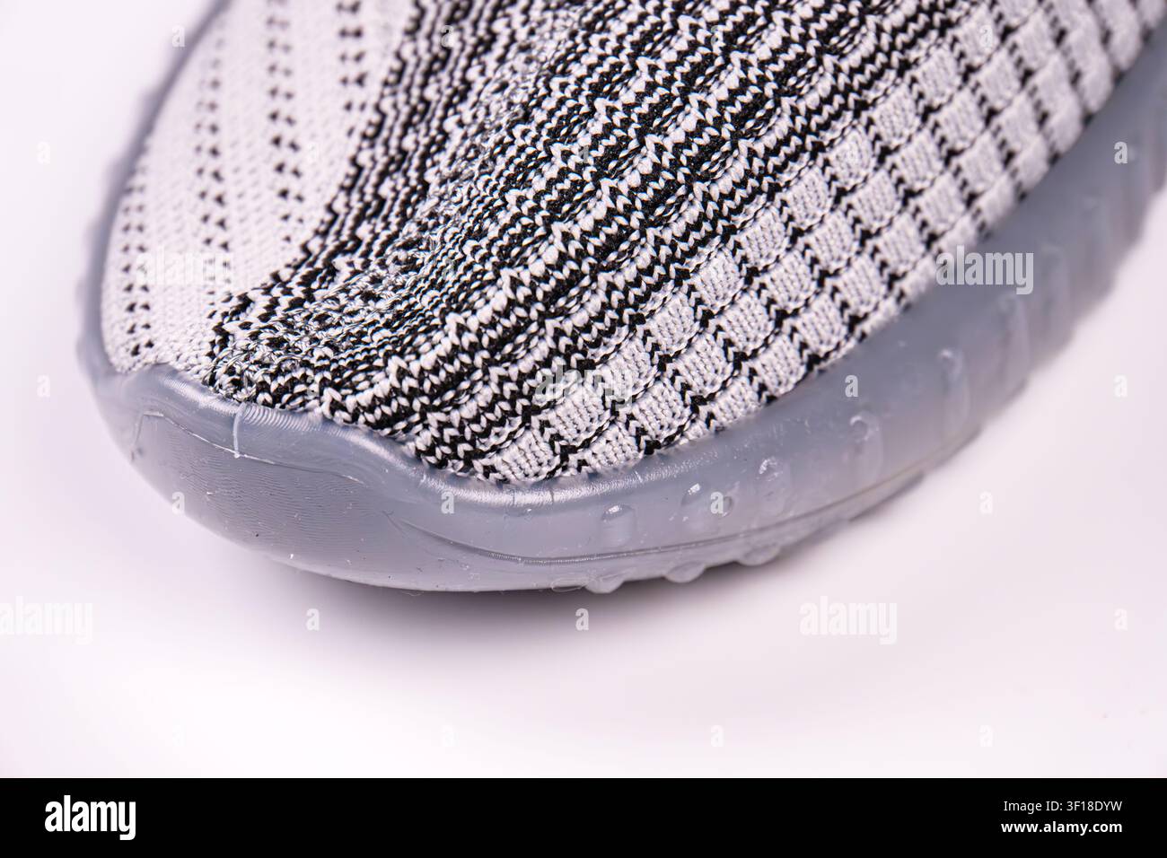 Close-up of modern shoe, showcasing knitted upper material, intricate pattern, translucent rubber sole, high-quality construction, studio lighting, cl Stock Photo
