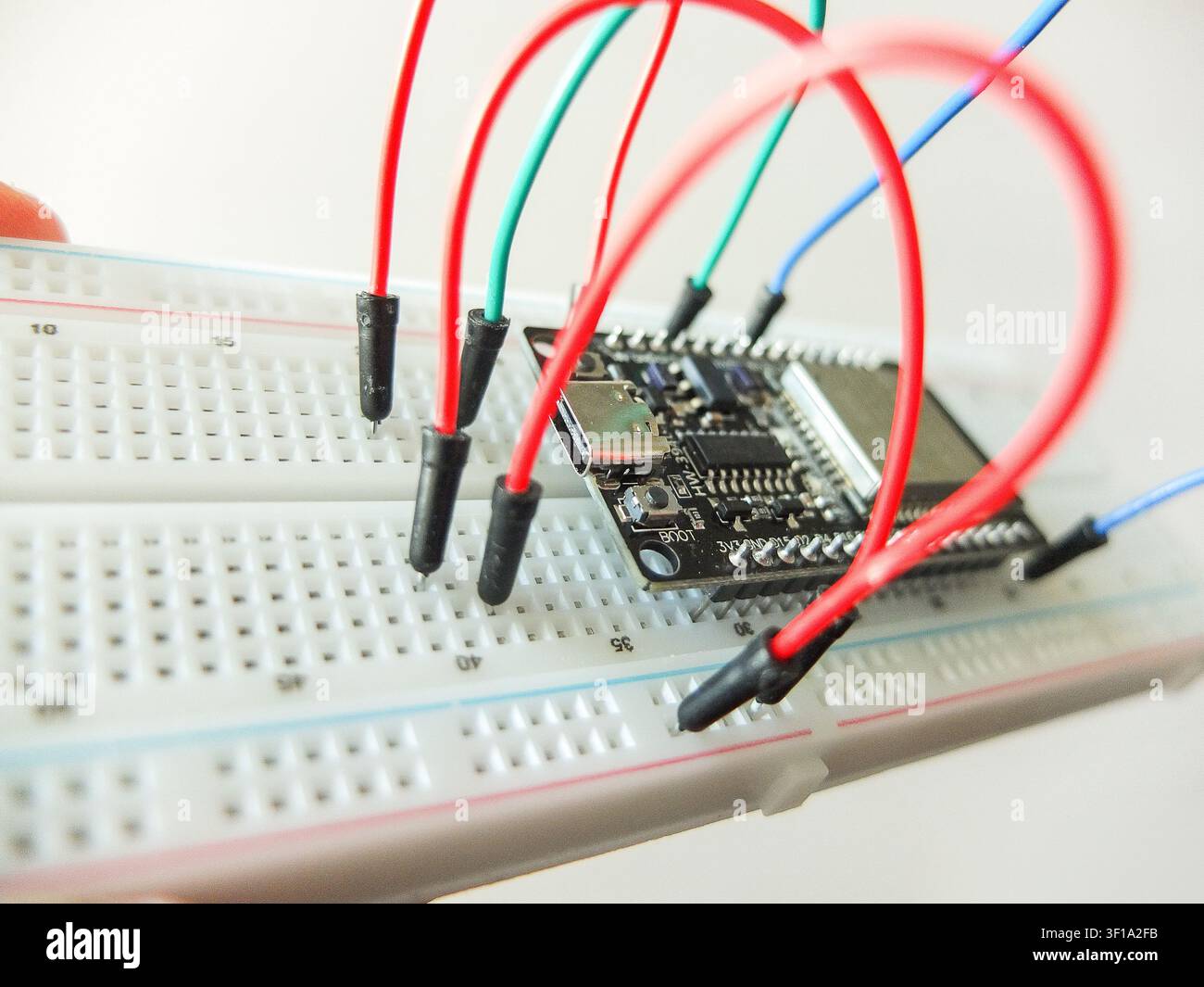Microcontroller board with connected colorful jumper wires on electronic breadboard. Stock Photo