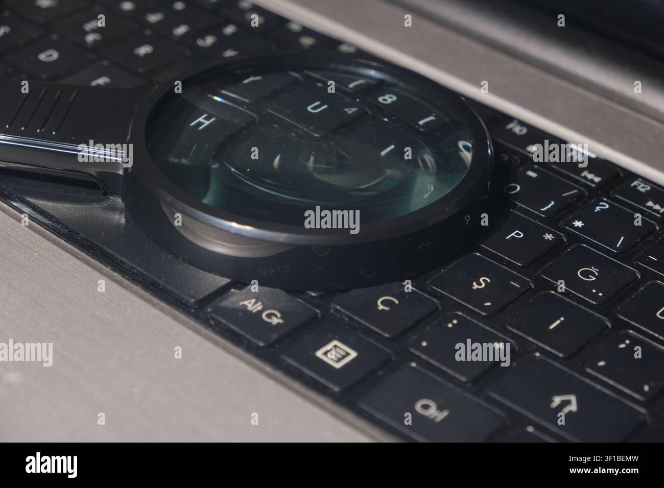 Magnifying glass hovering over a modern computer keyboard close-up Stock Photo