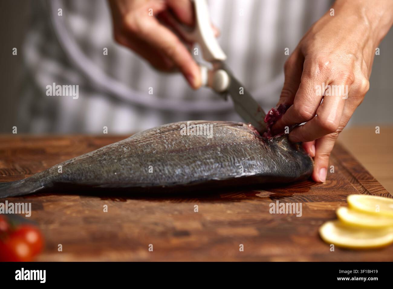 Hands cutting fresh raw sea bream on wooden board Stock Photo
