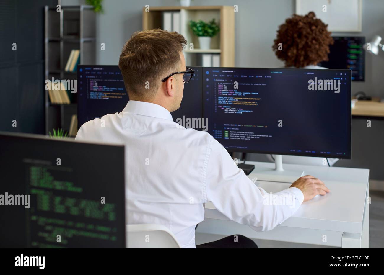 Programmer coding at dual monitors in collaborative modern software office Stock Photo