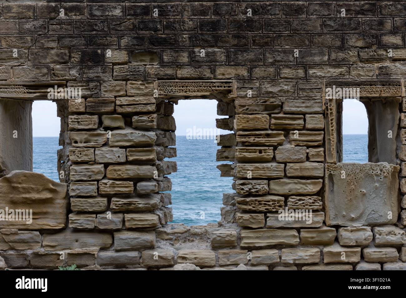 Weathered ancient stone wall with rectangular openings overlooking the sea. Stock Photo