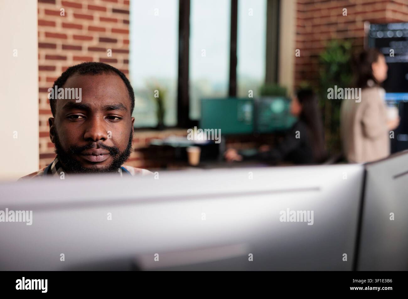 African American programmer develops a scalable security application in a software office, working with advanced technology and layered digital systems. Stock Photo