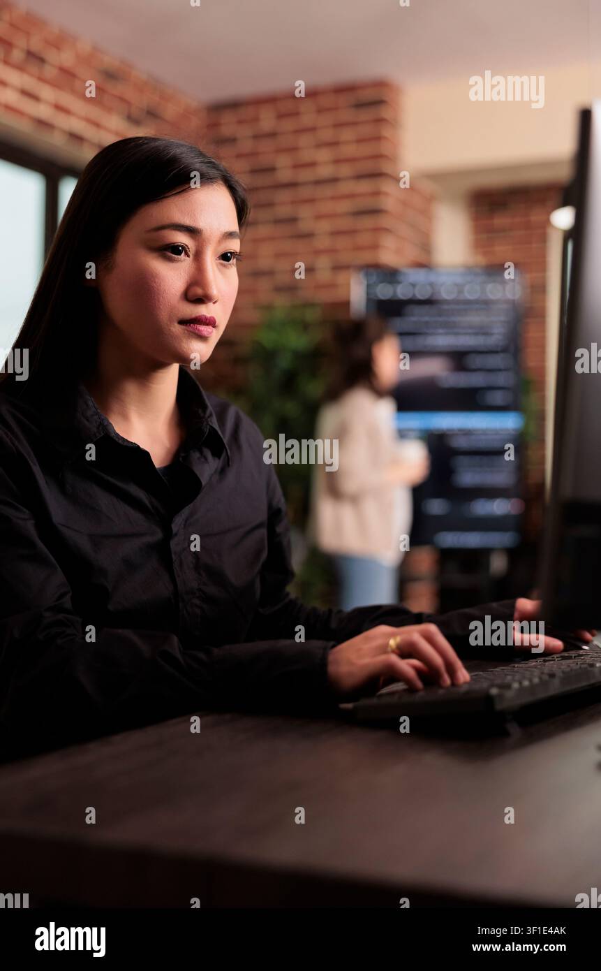 Asian developer checking HTML script on computer terminal while developers work with code, terminal windows and digital systems in an IT office focused on software production. Stock Photo