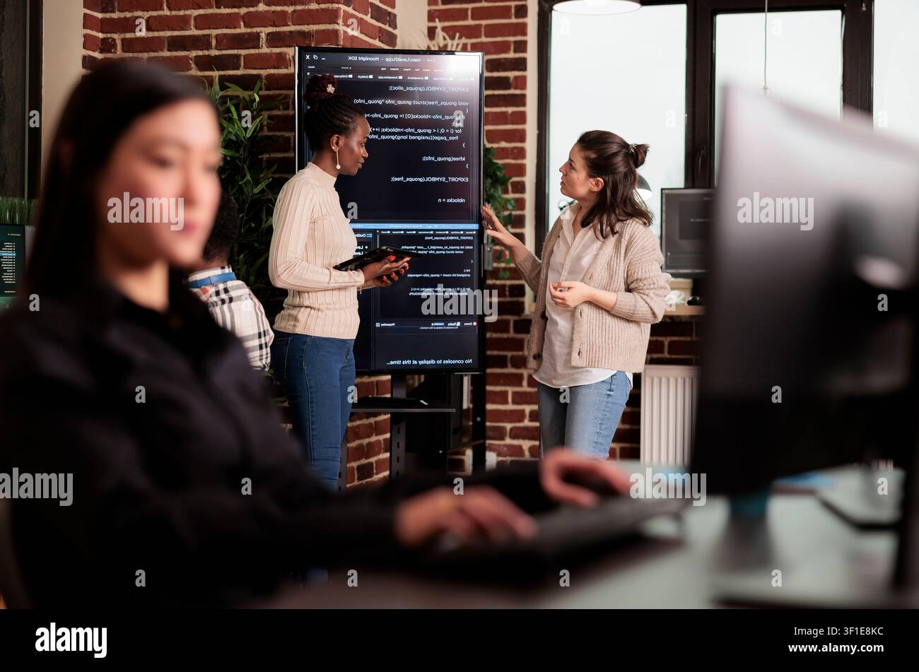 Diverse engineers discuss algorithms on screen, connecting programming code, software teamwork and digital infrastructure during a collaborative IT project. Stock Photo