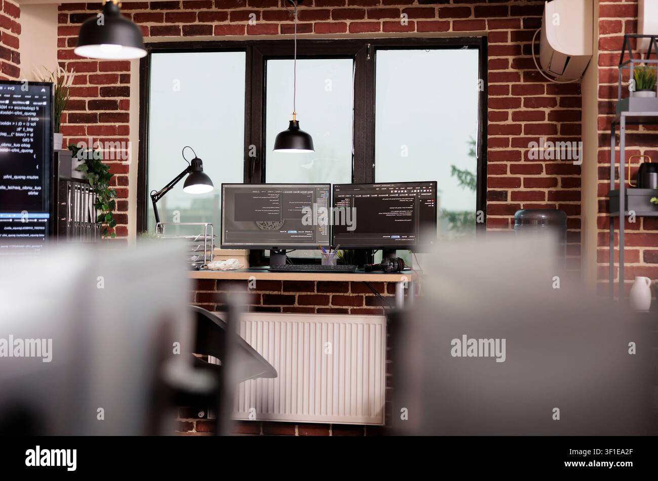 Desk with multiple monitors runs terminal windows and database scripts in an empty programming office focused on cloud computing and system code. Stock Photo