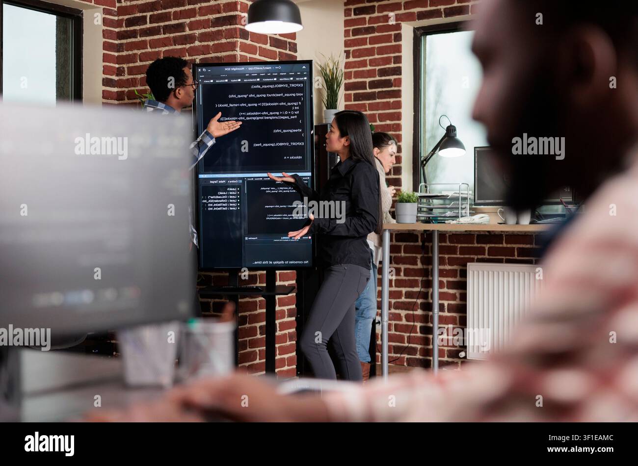 Software developers stand near a vertical screen while discussing an interface bug, slow processing and database security code review, as a software engineering and data workflow scene. Stock Photo